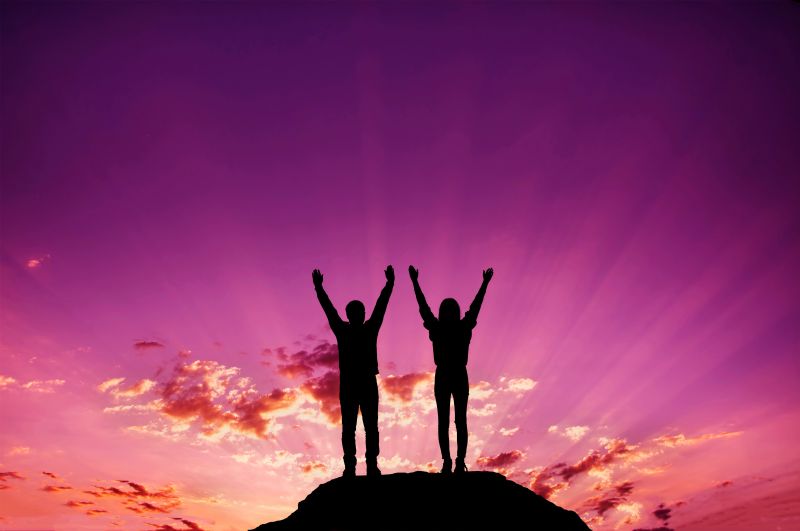 two people with arms raised on hill